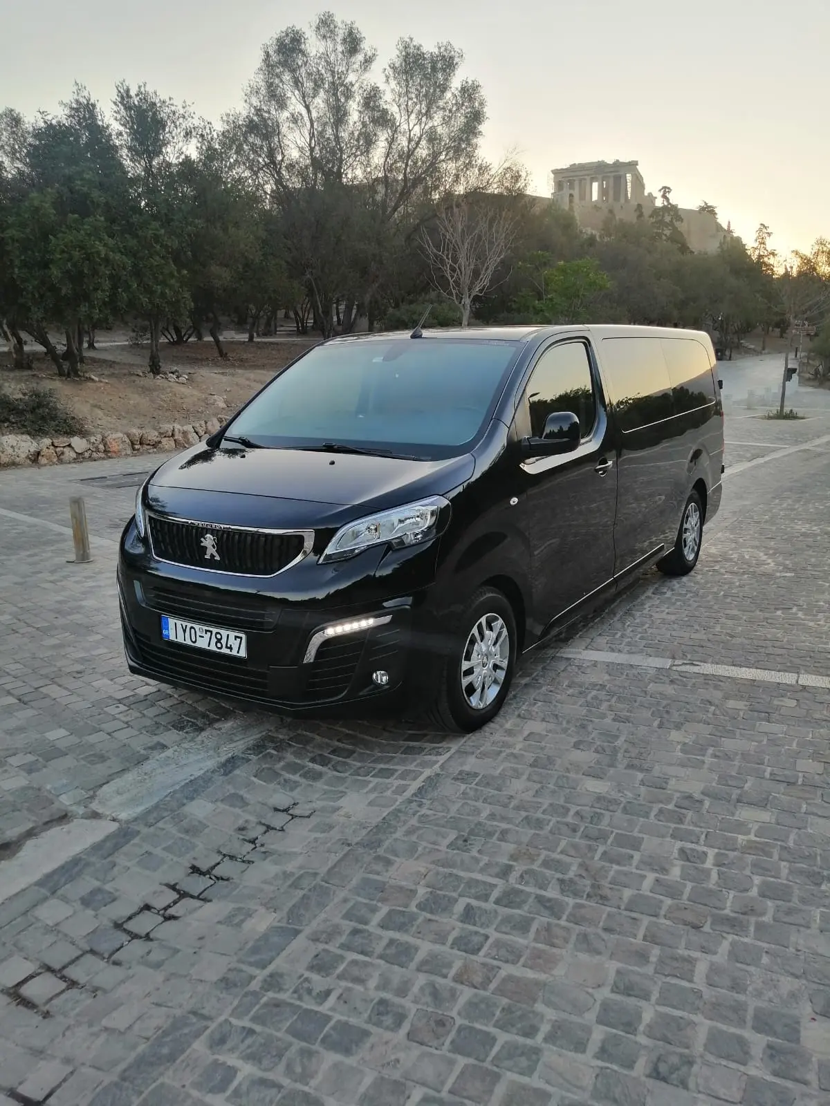 Attica Transfer Peugeot Traveller mini van parked below the Acropolis at sunset